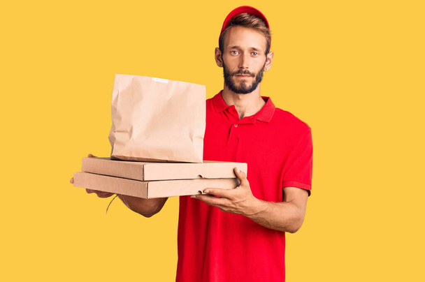 Handsome blond man with beard holding take away food thinking attitude and sober expression looking self confident  - Photo, Image