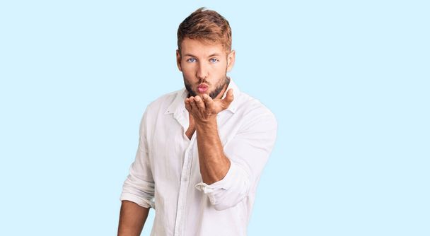 Young caucasian man wearing casual clothes looking at the camera blowing a kiss with hand on air being lovely and sexy. love expression.  - Photo, Image