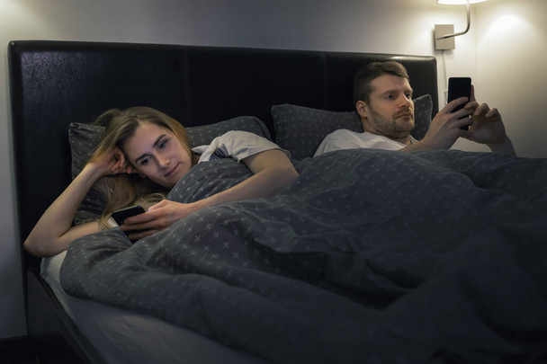 結婚した夫婦はベッドでスマートフォンを使って互いを無視した。関係ルーチン通信の問題インターネット中毒の概念 - 写真・画像