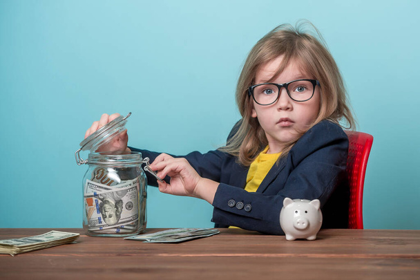 Portrait of child who steals money from parent savings. Adorable young girl wants to be rich. Kid in glasses can count money. - Photo, image