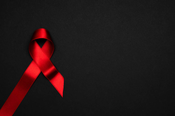 Dia da SIDA. Símbolo de fita vermelha no dia mundial de hiv no fundo escuro. Auxílios de conscientização e câncer. Conceito médico e de saúde - Foto, Imagem