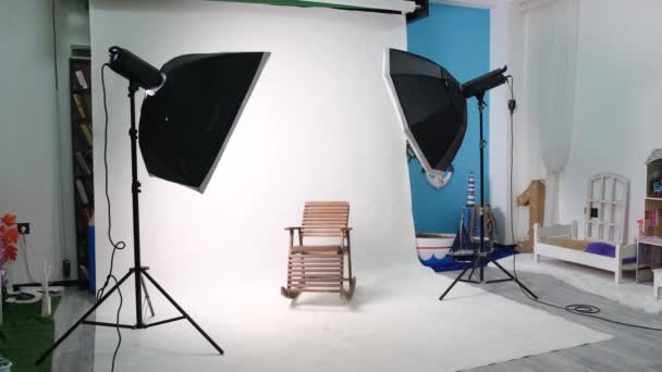 Studio fotograficzne lub wideo z dwoma sześciokątnymi lampami studyjnymi. Biały ekran i fotel bujany - Materiał filmowy, wideo