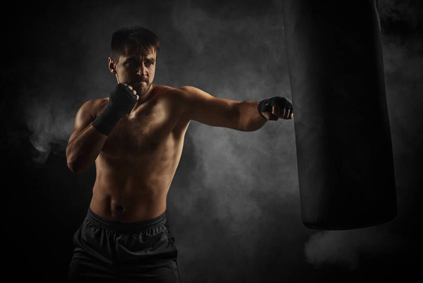 boxer in black boxing wraps punching in boxing bag - Фото, зображення