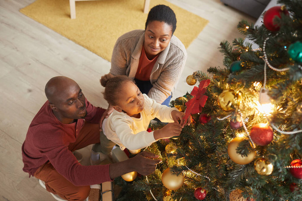 Alto angolo ritratto di carina ragazza afro-americana decorare l'albero di Natale con la famiglia amorevole mentre si gode la stagione delle vacanze a casa - Foto, immagini