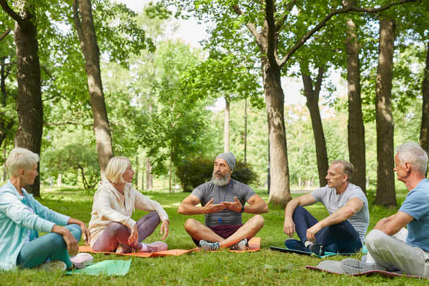 Vue d'ensemble de entraîneur de yoga professionnel démontrant à ses clients seniors comment faire de l'exercice de respiration - Photo, image