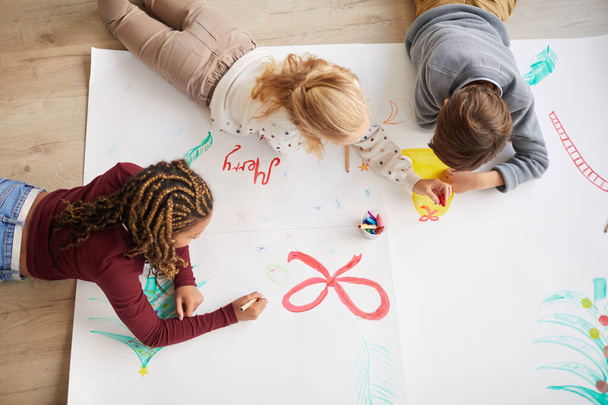 Vue de dessus à un groupe multi-ethnique d'enfants dessinant des images sur le sol tout en profitant d'un cours d'art à Noël, espace de copie - Photo, image