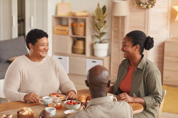 アフリカ系アメリカ人の家族の温かいトーンの肖像画居心地の良いインテリアで自宅で朝食を食べながらお茶や軽食を楽しんで - 写真・画像