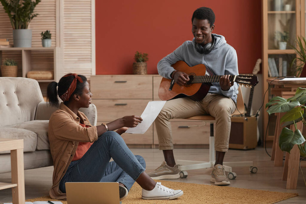 Full length portrait of two young African-American musicians playing guitar and writing music together in home recording studio - Valokuva, kuva