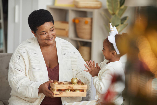 Afro-Amerikan büyükanne portresi Noel ağacını küçük tatlı bir kızla süslerken tatil sezonunun tadını çıkarıyor. - Fotoğraf, Görsel