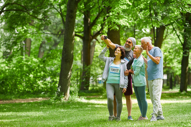Gruppe fröhlich sportlicher erwachsener Senioren steht zusammen im Park und macht ein Gruppenselfie mit der Smartphone-Kamera - Foto, Bild