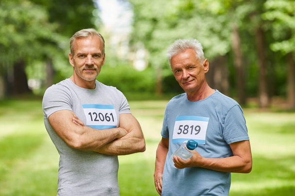 Середній портрет двох привабливих дорослих чоловіків, учасників літнього марафону, що стоять разом, дивлячись на камеру
 - Фото, зображення