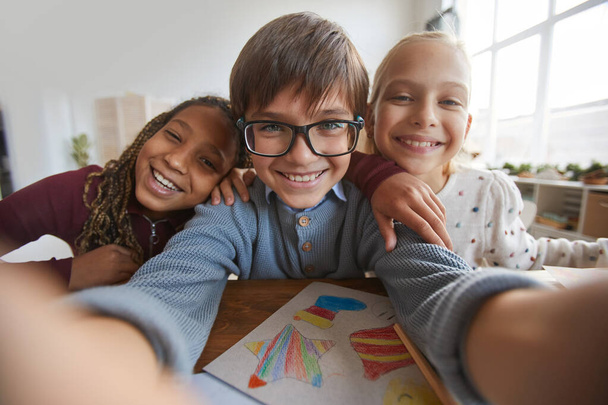 Retrato de tres niños felices sonriendo a la cámara mientras toman fotos de selfies en la escuela - Foto, imagen