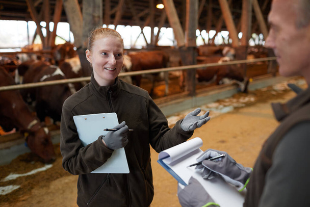 Високий кут зору на двох працівників, які говорять, стоячи у тваринництві на сімейній фермі, копіювати простір
 - Фото, зображення