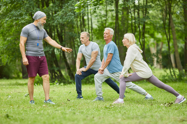 Profesionální fitness trenér pracující v městském parku s aktivními starými lidmi je opravuje při cvičení - Fotografie, Obrázek