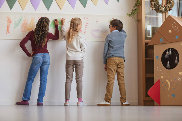 Vista trasera en el grupo multiétnico de niños dibujando en las paredes mientras disfruta de clases de arte en la escuela, espacio para copiar - Foto, Imagen