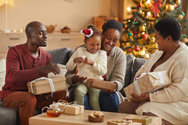 家庭でホリデーシーズンを楽しみながらクリスマスプレゼントを開く幸せなアフリカ系アメリカ人の家族の暖かいトーンの肖像画 - 写真・画像