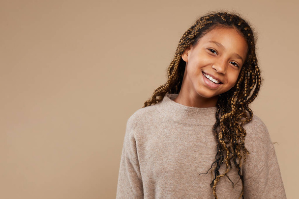 Porträt eines unbeschwerten afroamerikanischen Mädchens, das glücklich in die Kamera lächelt, während es vor beigem Hintergrund im Studio steht, Kopierraum - Foto, Bild