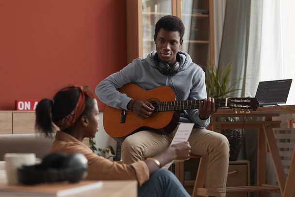 Προσωπογραφία δύο νεαρών Αφροαμερικανών μουσικών που παίζουν κιθάρα και γράφουν μουσική μαζί στο στούντιο ηχογράφησης στο σπίτι - Φωτογραφία, εικόνα