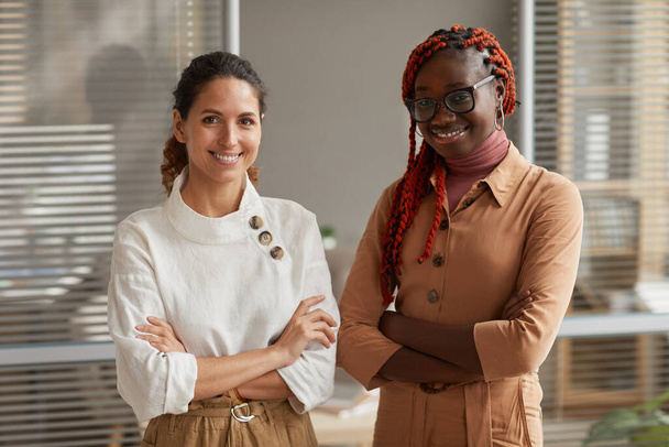 Waist up portrait of two successful young businesswomen smiling at camera while posing confidently standing with arms crossed in office, copy space - Photo, Image