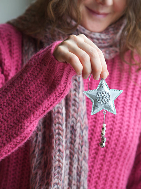 Joven mujer caucásica sonriente en suéter rosa y silenciador que sostiene la estrella - decoración de Navidad blanca. Concepto de Navidad con espacio de copia. - Foto, imagen