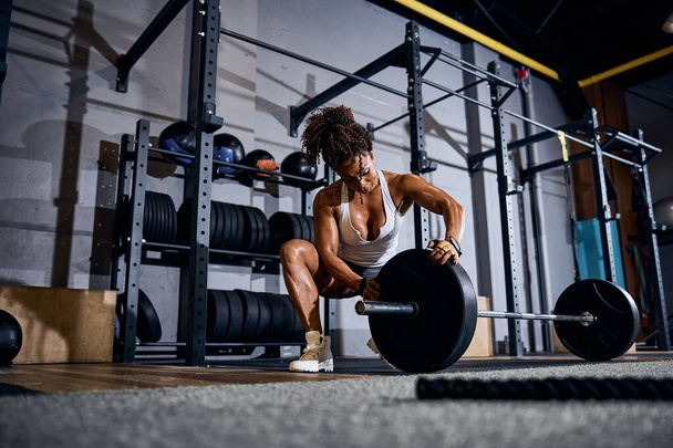 Female weightlifter loading the barbell before the training session - Foto, imagen