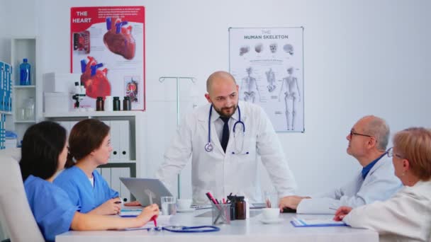 Profesjonalny lekarz stojący przed kolegami przedstawiającymi dokumentację medyczną - Materiał filmowy, wideo