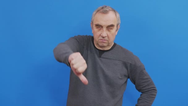 Sad man in basic casual blue t-shirt isolated on blue background studio. People emotions lifestyle concept. Looking camera showing pointing fingers down. - Footage, Video