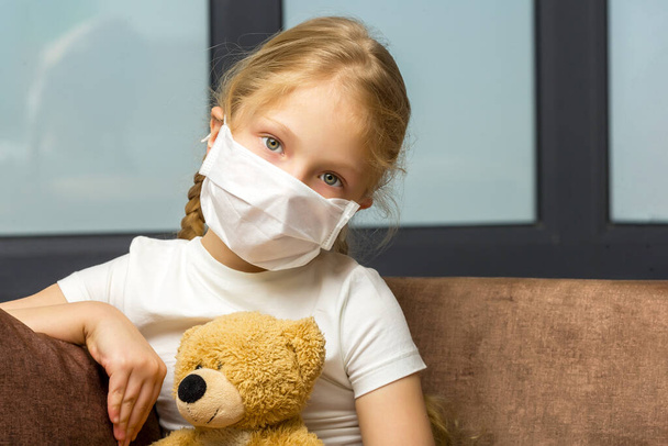 Little girl in a medical mask hugs a teddy bear. covid concept. - Photo, Image