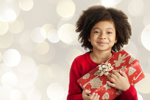 ritratto di una bambina sorridente con i capelli ricci che regge un regalo di Natale  - Foto, immagini