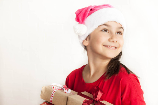 das kleine Mädchen mit dem Weihnachtsmannhut hält Geschenkschachteln - Foto, Bild