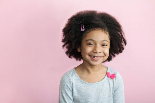 портрет улыбающейся маленькой девочки с вьющимися волосами в студии - Фото, изображение