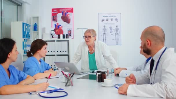 Vanhempi naislääkäri seisoo kollegoiden edessä, jotka esittävät diagnoosin - Materiaali, video