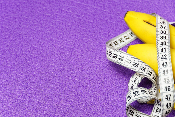 Primer plano de un racimo de plátanos y una cinta métrica sobre un fondo púrpura. Estilo de vida saludable y nutrición adecuada. - Foto, imagen