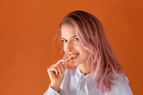 A young woman with pink hair eats fried potato slices, French fries. - Photo, image