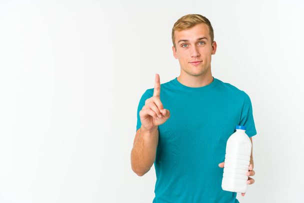 Fiatal kaukázusi férfi iszik tej elszigetelt fehér háttér mutatja első számú ujját. - Fotó, kép