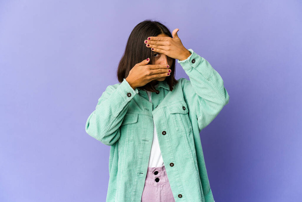 Young mixed race woman blink at the camera through fingers, embarrassed covering face. - Photo, Image