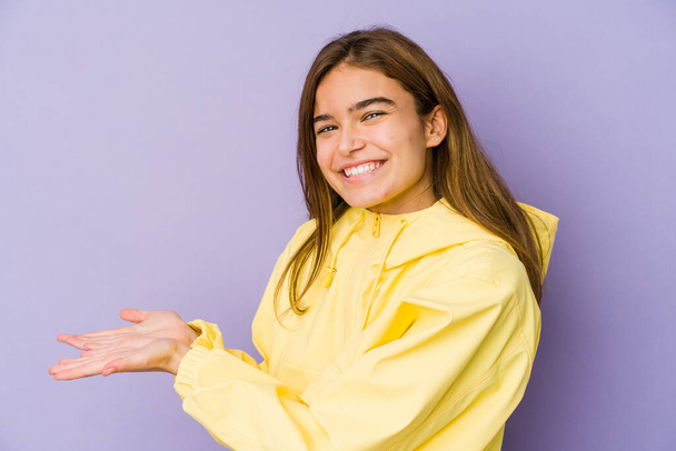 Young skinny caucasian girl teenager on purple background holding a copy space on a palm. - Photo, image
