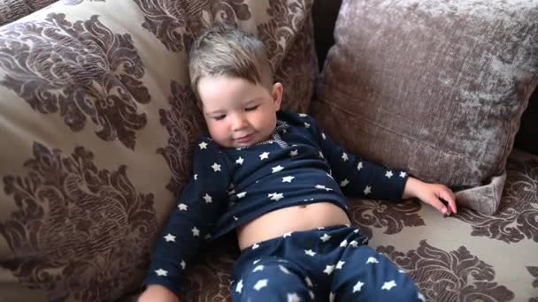 Un niño cansado descansa en el sofá. Bebé parpadeante mintiendo - Metraje, vídeo