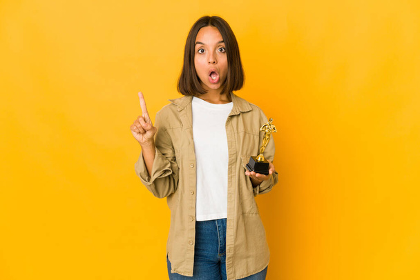Young hispanic woman holding an award statuette having some great idea, concept of creativity. - Foto, Imagen