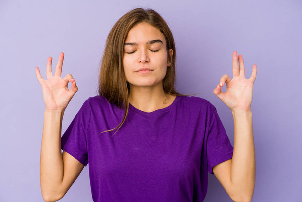 Young skinny caucasian girl teenager on purple background relaxes after hard working day, she is performing yoga. - Photo, Image