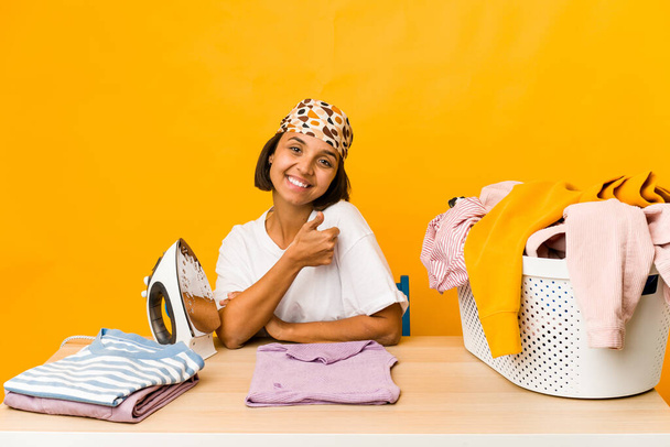 Молодая латиноамериканка гладит одежду изолированно улыбаясь и поднимая большой палец вверх - Фото, изображение