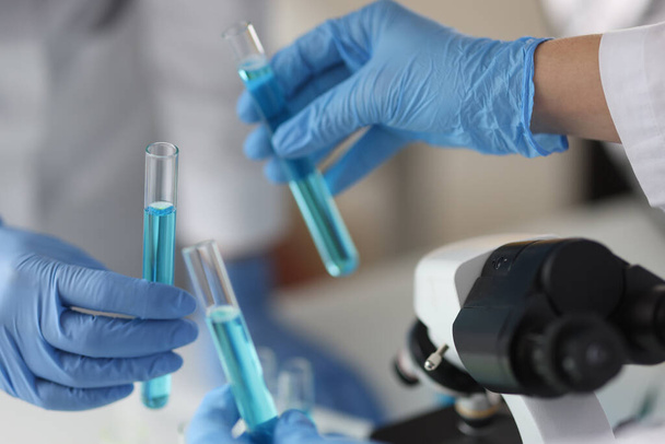 Manos en guantes de goma protectores sosteniendo en tubo de ensayo con líquido azul en laboratorio - Foto, Imagen