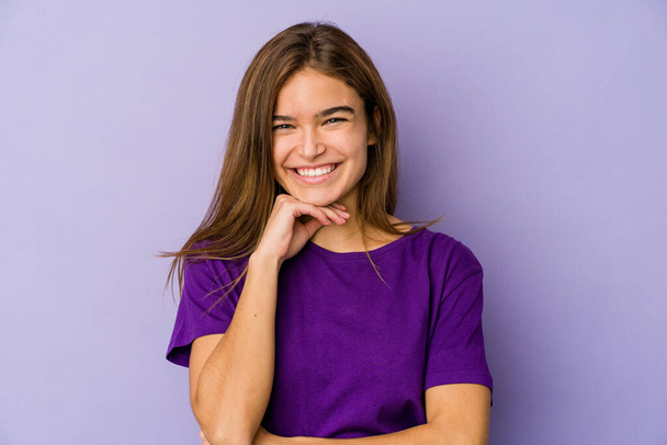 Jeune adolescente caucasienne maigre sur fond violet souriant heureux et confiant, toucher le menton avec la main. - Photo, image