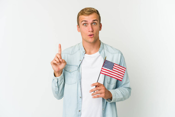Junger kaukasischer Mann mit amerikanischer Flagge auf weißem Hintergrund, der eine großartige Idee, ein Konzept der Kreativität hat. - Foto, Bild