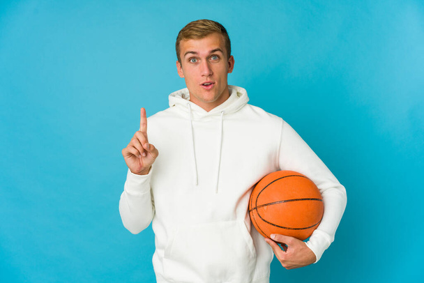 青い背景に孤立したバスケットボールをしている若い白人男性は素晴らしいアイデア、創造性の概念を持っています. - 写真・画像