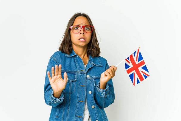 Beyaz arka planda İngiliz bayrağı tutan genç Latin kadın, yakın bir tehlike nedeniyle şok oluyor. - Fotoğraf, Görsel