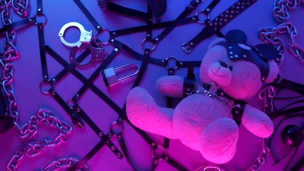 toy bear dressed in leather belt harness accessory for BDSM games on a dark background in neon light in the smoke - Footage, Video