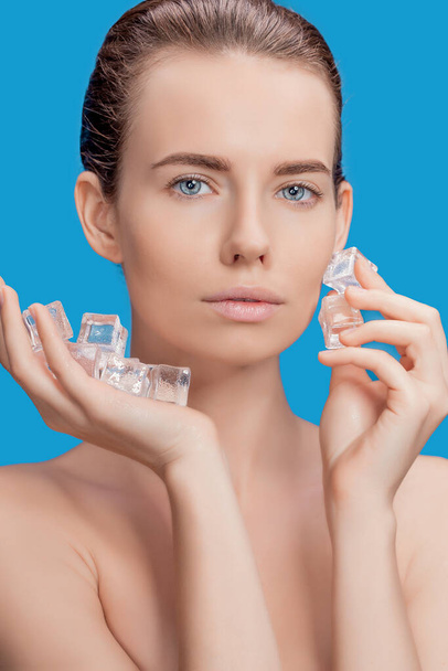 Beautiful woman applying ice cube treatment on blue background - Foto, Imagen