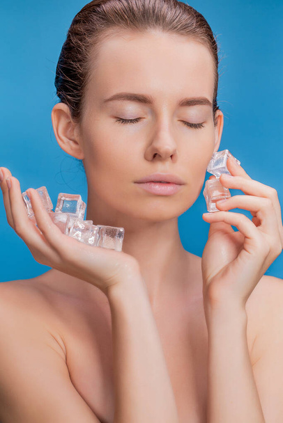 Beautiful woman applying ice cube treatment on blue background - Foto, afbeelding
