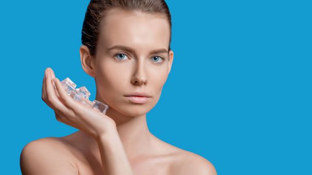 Beautiful woman applying ice cube treatment on blue background - Foto, immagini